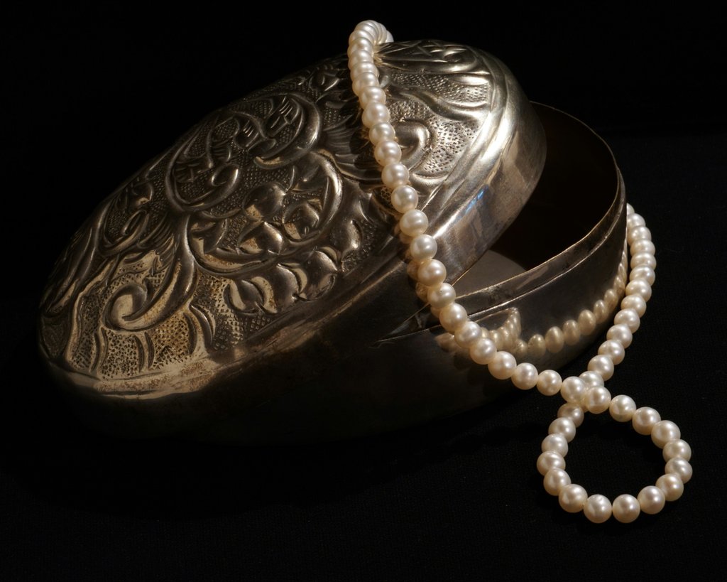 A string of white pearls draped over an ornate silver jewelry box against a dark background. A delicate, meaningful keepsake to honor a loved one’s memory."